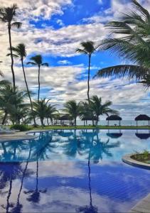 una piscina con palmeras y un cielo nublado en Flat Beira Mar Ancorar Porto de Galinhas, en Porto de Galinhas