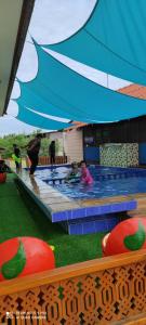 un groupe d'enfants jouant dans une piscine sous un parasol dans l'établissement HOMESTAY Kb Wakaf Kayu, à Kota Bharu