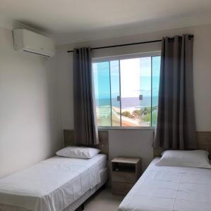 two beds in a room with a large window at Residencial Galápagos in Imbituba