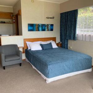 a bedroom with a bed and a chair and a window at Ala Moana Motel in Paihia
