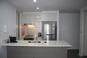 La cuisine est équipée de placards blancs et d'un réfrigérateur en acier inoxydable. dans l'établissement North Sydney Wyndel Apartments-MIL1005, à Sydney