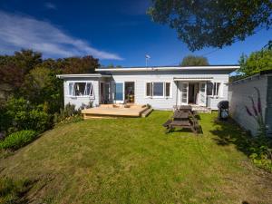 a white cottage with a deck and a yard at Incredible Bay Views - Kaiteriteri Bach in Kaiteriteri
