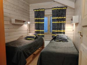 two beds in a room with wooden walls and windows at Levikaira Apartments - Log Cabins in Levi