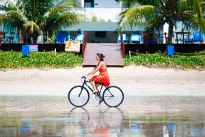 a woman in a red dress riding a bike in the water at Sollaris Ecopousada in Japaratinga