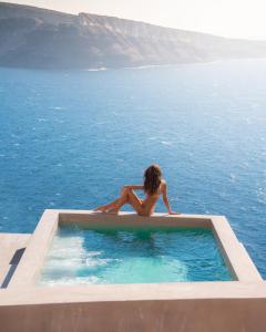 une femme assise dans une piscine à l'eau dans l'établissement Old Castle Oia, à Oia