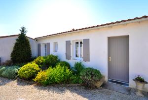 ein weißes Haus mit einer Tür und ein paar Büschen in der Unterkunft Maison de 2 chambres a Le Bois Plage en Re a 400 m de la plage avec piscine partagee terrasse amenagee et wifi in Le Bois-Plage-en-Ré