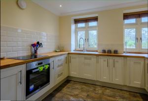 a large kitchen with white cabinets and windows at Sloley Hall Cottages - Stable 1 in Tunstead