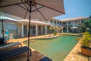 a swimming pool with an umbrella and a building at Santa Fe Motel and Holiday Units in Lennox Head