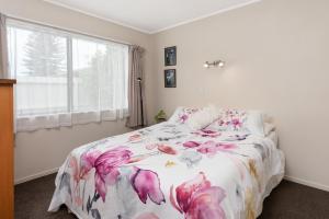a bedroom with a bed with a floral bedspread and a window at The Mount Beach Pad - Mt Maunganui Holiday Home in Matapihi