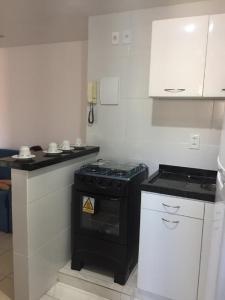 una pequeña cocina con estufa negra y armarios blancos. en Hospedagem da Rose - Cabo Frio, en Cabo Frío
