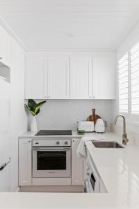 a white kitchen with a stove and a sink at The Bungalows at Bondi in Sydney