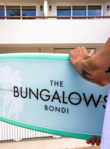 a man standing next to a sign that reads the bunakenaken board at The Bungalows at Bondi in Sydney