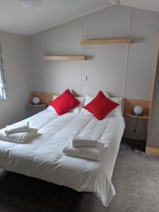 a bedroom with a white bed with red pillows at Caravan nearby Hastings Coghurst Hall Park in Guestling