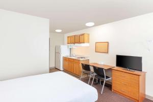 スーフォールズにあるWoodSpring Suites Sioux Fallsのベッド、デスク、キッチンが備わるホテルルームです。