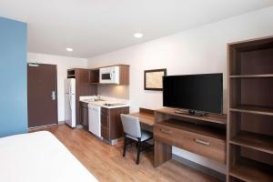 a room with a desk with a television and a kitchen at WoodSpring Suites Houston 288 South Medical Center in Houston