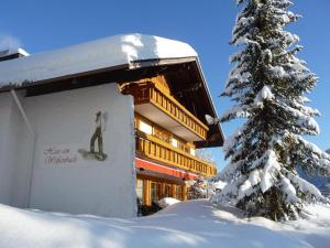 a building with a snowboard sign next to a snow covered tree at Haus am Weißenbach in Bad Hindelang