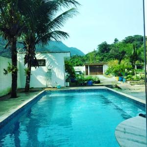 una piscina azul con una palmera y una casa en Takeo's House, en Boicucanga