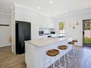 a white kitchen with a white counter and stools at Salty Shores Jervis Bay I 3 Mins to Beach in Callala Beach