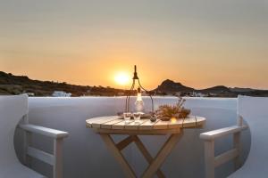 White Tinos Luxury Suites في Stení: طاولة مع شموع ومصباح على طاولة في شرفة مع غروب الشمس