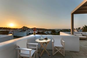 White Tinos Luxury Suites في Stení: طاولة وكراسي على شرفة مع غروب الشمس