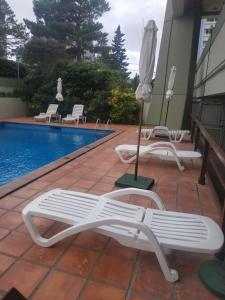 zwei Liegestühle und ein Sonnenschirm neben einem Pool in der Unterkunft Apartamento Marina de roosvelt con piscina climatizada in Punta del Este