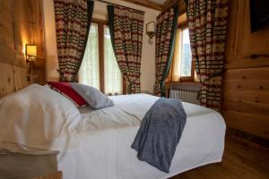 1 dormitorio con 1 cama blanca en una habitación con ventanas en Laghetto Alpine Hotel & Restaurant, en Brusson