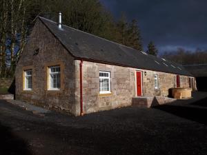 un antiguo edificio de piedra con una puerta roja y ventanas en Inviting 2-Bed Barn with hot tub near Muirkirk, en Cumnock