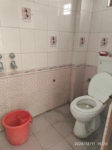 a bathroom with a toilet and a red bucket at Yogi Home Stay in Rishīkesh