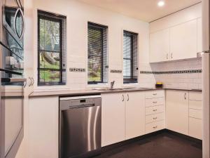 a kitchen with white cabinets and a stainless steel dishwasher at Village Green 2 Bedroom loft townhouse with views fireplace and garage parking in Thredbo