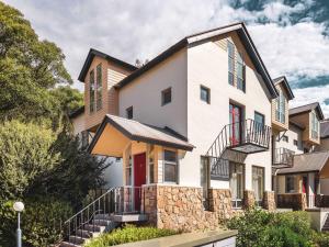 a large white house with a stone wall at Village Green 2 Bedroom loft townhouse with views fireplace and garage parking in Thredbo