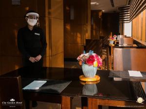 um homem usando uma máscara facial e um vaso de flores em uma mesa em City Garden Hotel Makati em Manilla