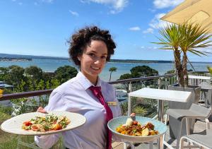 una mujer sosteniendo dos platos de comida en un balcón en Harbour Heights Hotel, en Poole