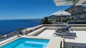 a swimming pool with chairs and an umbrella and the ocean at Blue Views Villas and Apartments in Cape Town