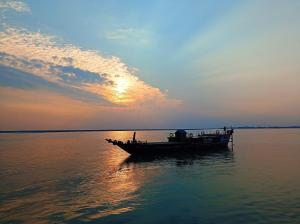 un barco en medio del agua al atardecer en MAHESWAR LAND, en Majuli