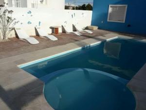a blue swimming pool with a row of white chairs at Aguamarina in Las Grutas