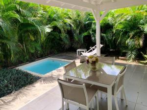 a table and chairs under an umbrella next to a pool at Appartement confortable au Moule 60 m² avec piscine privée in Le Moule