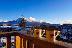 two coffee mugs sitting on a wooden railing with mountains at Rando, ski & lac, grand appartement 6 personnes - Lac de Serre ponçon in Prunières