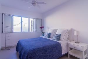 een witte slaapkamer met een bed met een blauwe deken bij Rooms & Suites Princesa Leticia in Puerto del Carmen