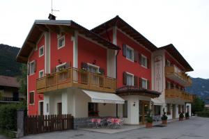 a red building with a balcony and tables at Hotel Dolomiti Saone in Tione di Trento