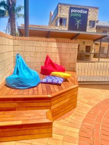 tres bolsas coloridas sentadas en un banco de madera en Mulwala Paradise Palms Motel, en Mulwala