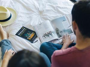 two women sitting on a bed reading books at Urban Apartments Melbourne on Elizabeth in Melbourne