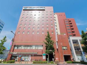 a tall red brick building with a tree in front of it at Tabist Hotel Tetora Kitakyushu in Kitakyushu
