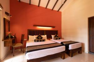 two beds in a room with a red wall at Mapakada Village - Mahiyanganaya in Mahiyangana