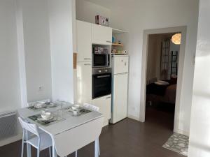 a white kitchen with a table and a white refrigerator at T1 40 m2. Lit Queen size in Pau