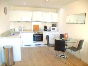cocina con armarios blancos, mesa y sillas en New Central Woking 1 and 2 Bedroom Apartments with Free Gym, close to Train Station en Woking