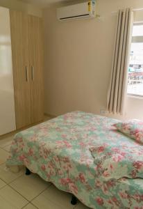 a bedroom with a bed with a floral comforter and a window at Edifício Iris - Bombinhas in Bombinhas