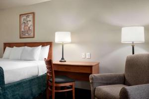 a hotel room with a bed, chair, lamp and a lamp post at Travelodge by Wyndham Clinton Valley West Court in Clinton