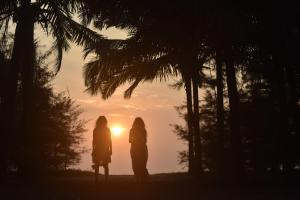 dos mujeres de pie en frente de la puesta de sol en Xandari Pearl Beach Resort, en Mararikulam