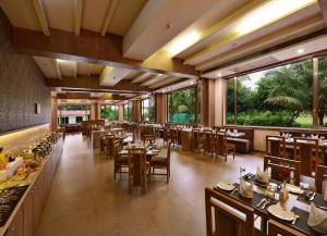 a restaurant with tables and chairs and large windows at Sarovar Portico Gir in Sasan Gir