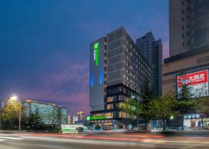 臨沂にあるHoliday Inn Express Linyi North New District, an IHG Hotelの夜間の緑の看板が立つ高層ビル